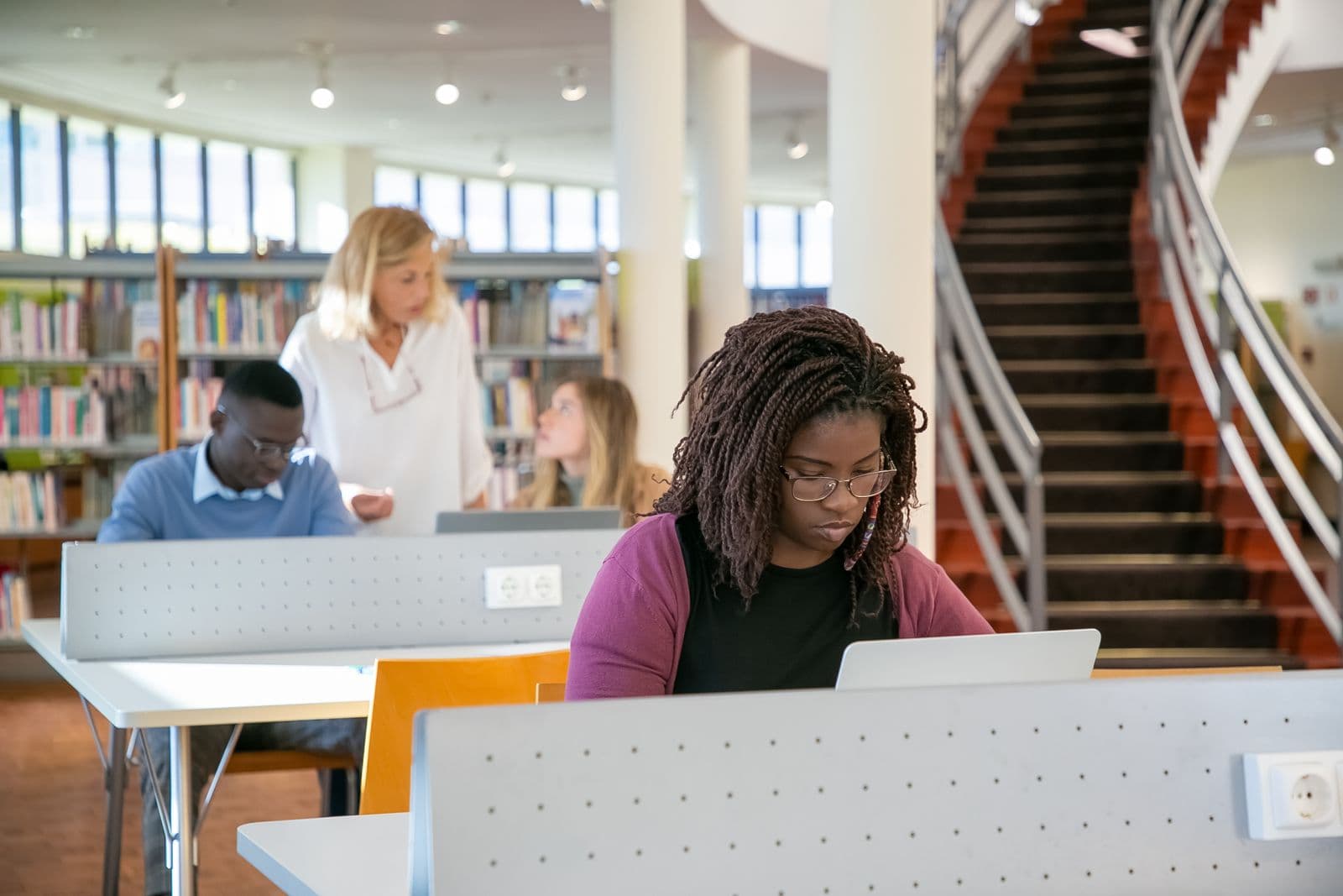 Learners working on laptops at a shared library desk